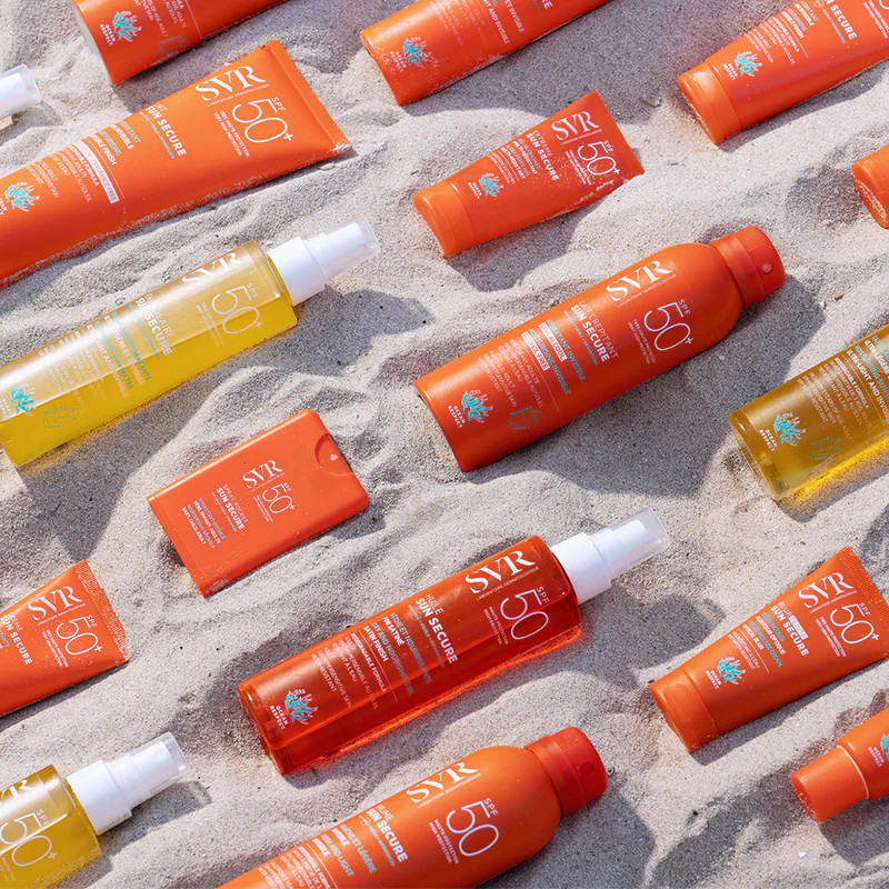 Assortiment de produits SVR Sun Secure disposés sur une plage de sable.