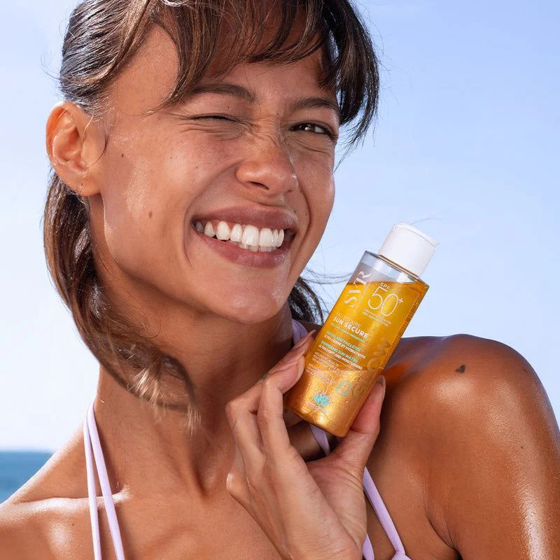 Femme tenant le flacon SVR Sun Secure Eau Solaire Glow SPF50+, souriante à la plage.