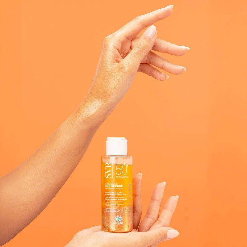 Mains de femme tenant un flacon de crème solaire SVR Sun Secure Eau Solaire Glow SPF50+.