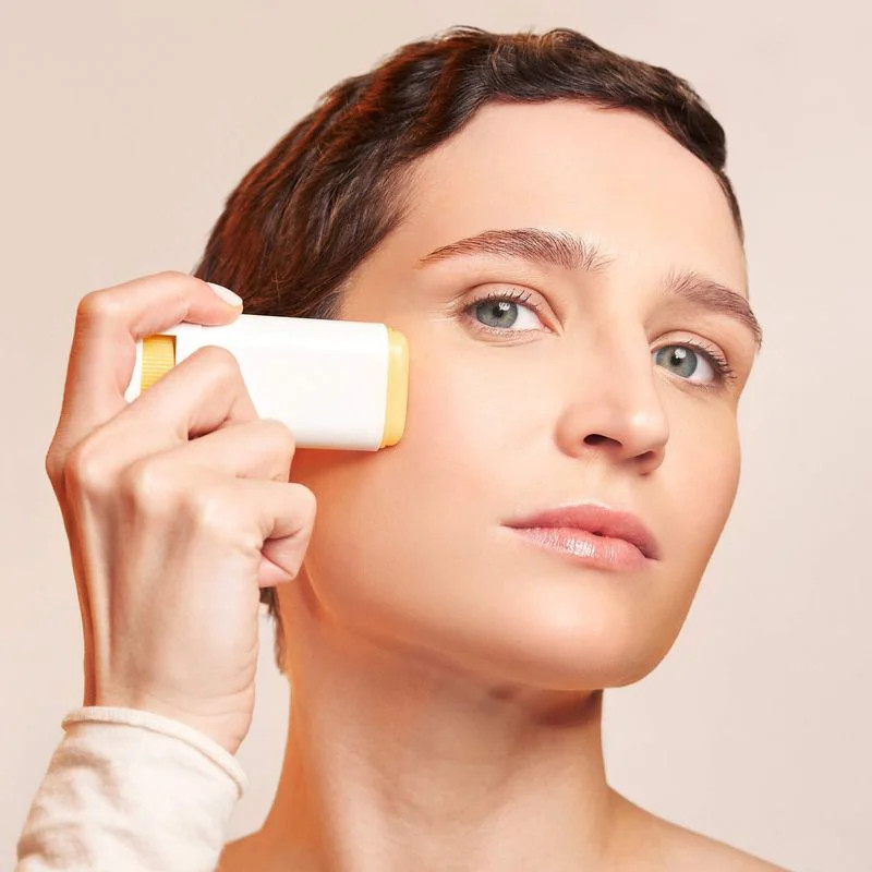 Femme appliquant le stick solaire MÊME SPF50+ sur son visage autour des yeux, démontrant une applica