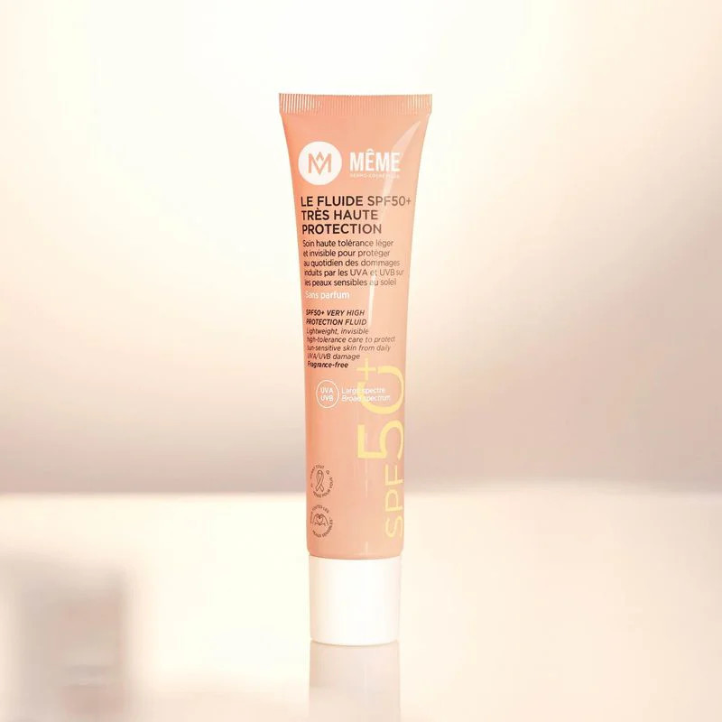 Gros plan ambient du tube de Fluide Solaire SPF50+ MÊME posé sur surface, mettant en valeur le desig