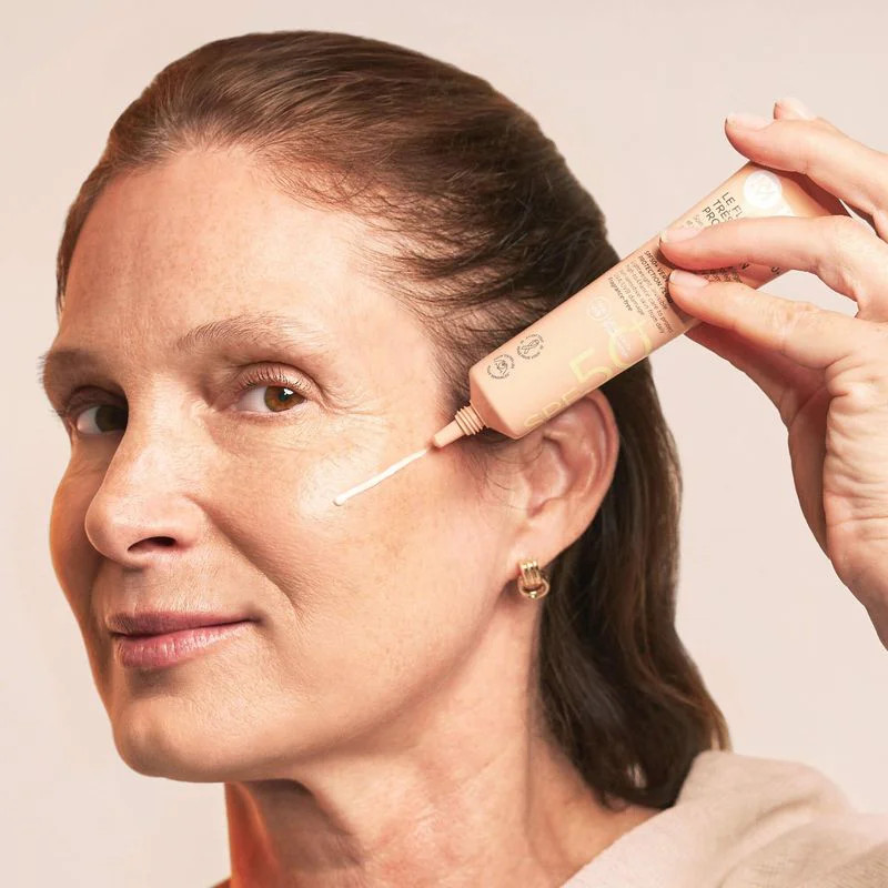 Femme appliquant le Fluide Solaire SPF50+ MÊME sur son visage avec tube, photo lifestyle montrant un