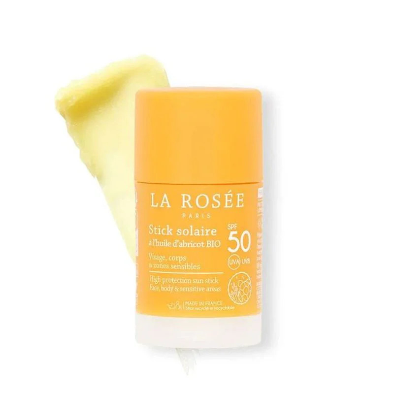 Stick solaire La Rosée SPF 50+ en emballage orange avec crème jaune appliquée sur le dessus, texture