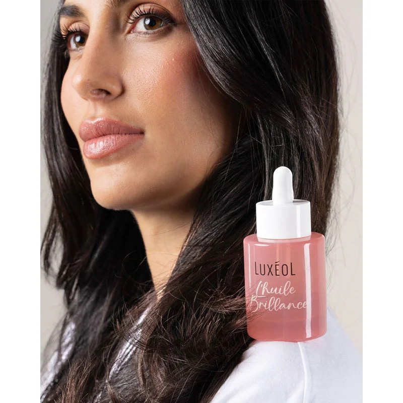 Femme en peignoir blanc tenant l'Huile Brillance Luxéol avec Shampoing Brillance, Masque et Sérum, c