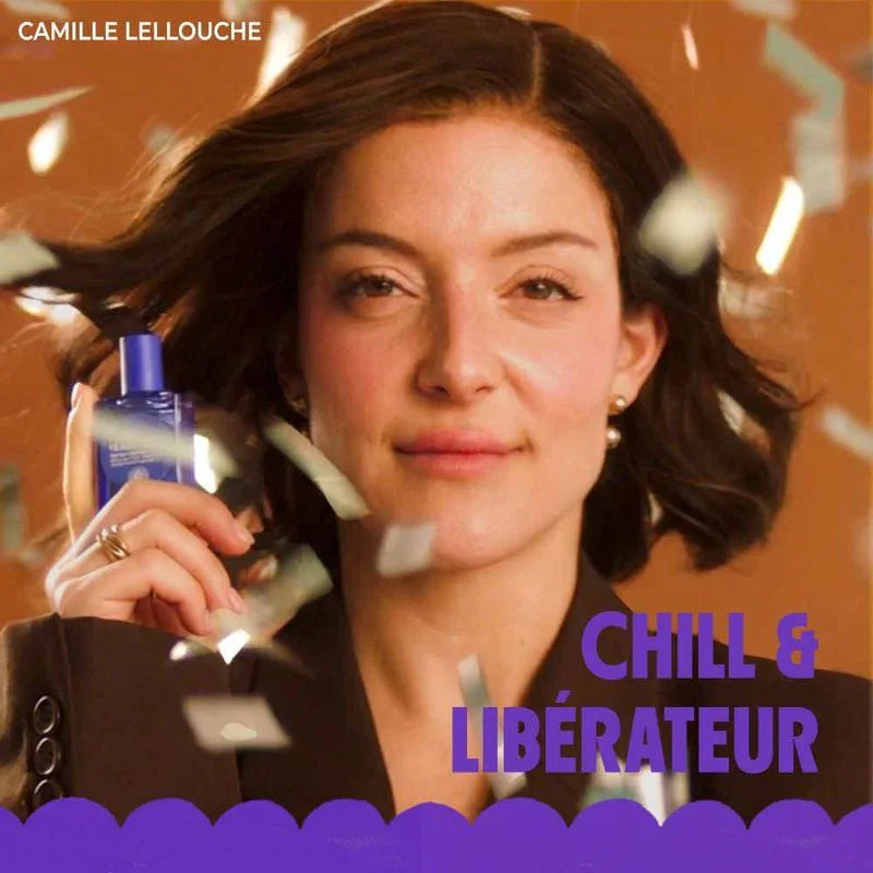 Femme tenant le flacon roll-on Café Roger entouré de fleurs rouges dans un cliché lifestyle vibrant,